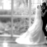 The bride and groom here are kissing in front of a window of a hallway at the Rosewood Crescent Hotel in Dallas Texas