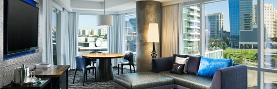 the cool corner room at the w hotel dallas texas has a sectional sofa with a flat screen tv along with a dining table for 4 and a private bedroom with a king bed